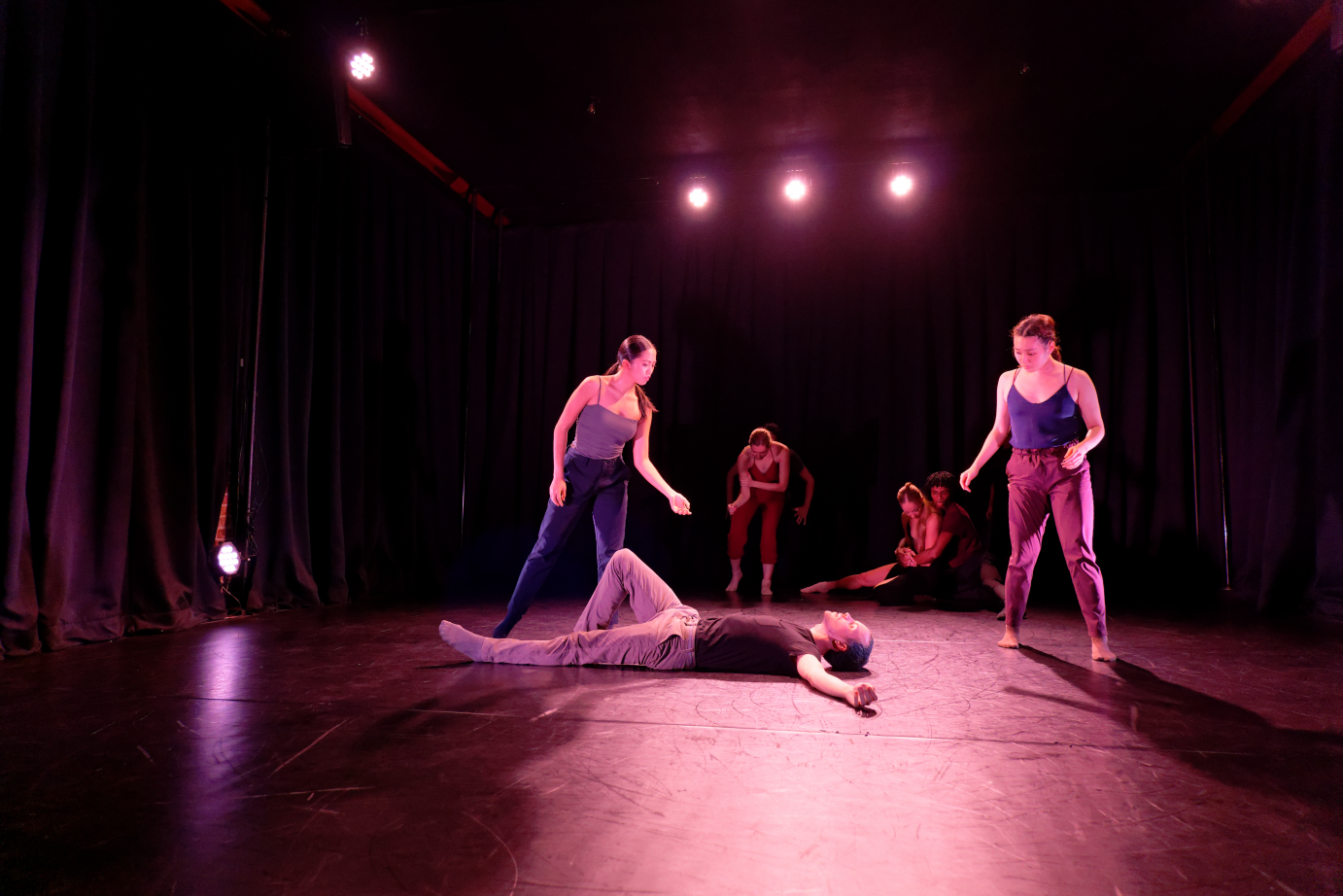 One dancer lies on the floor, with splayed arms akimbo and one knee bent. Two dancers hover over him. In the backbend, other dancers hold themselves.